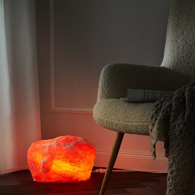 Zoutkristallenlamp straalt warm licht naast een comfortabele stoel.