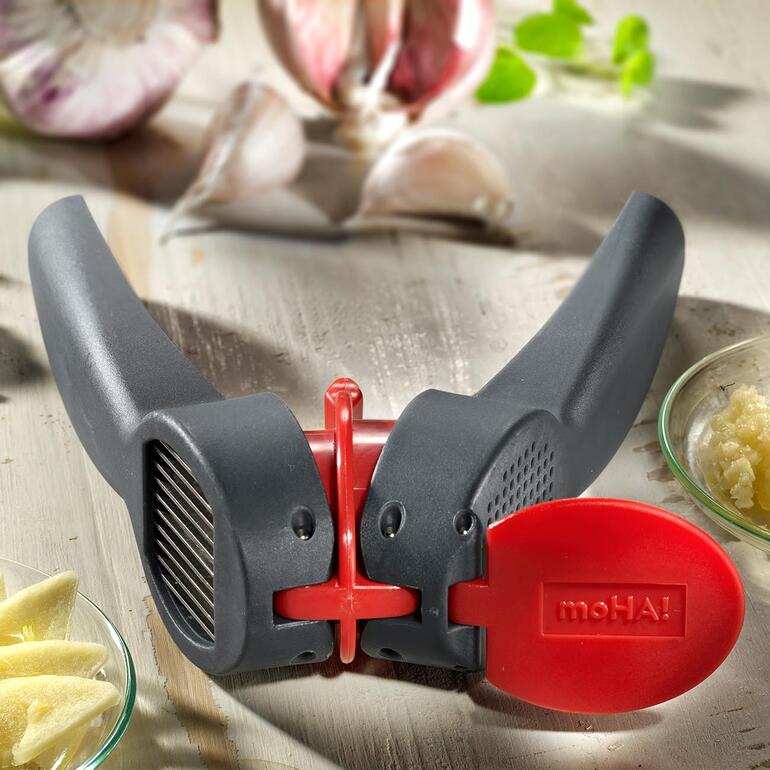 Knoflooksnijder en -pers in zwart met rode knop en knoflookteentjes op de achtergrond.