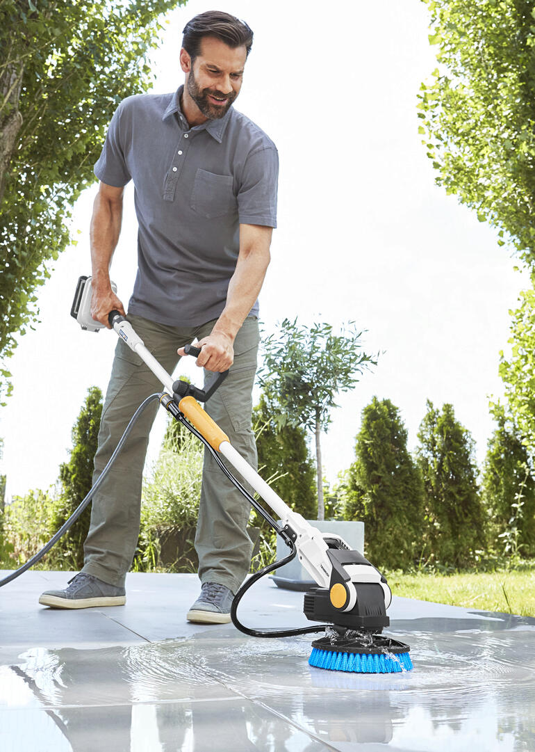 Man gebruikt de Twin Brush elektro-scrubber op een terras buiten.