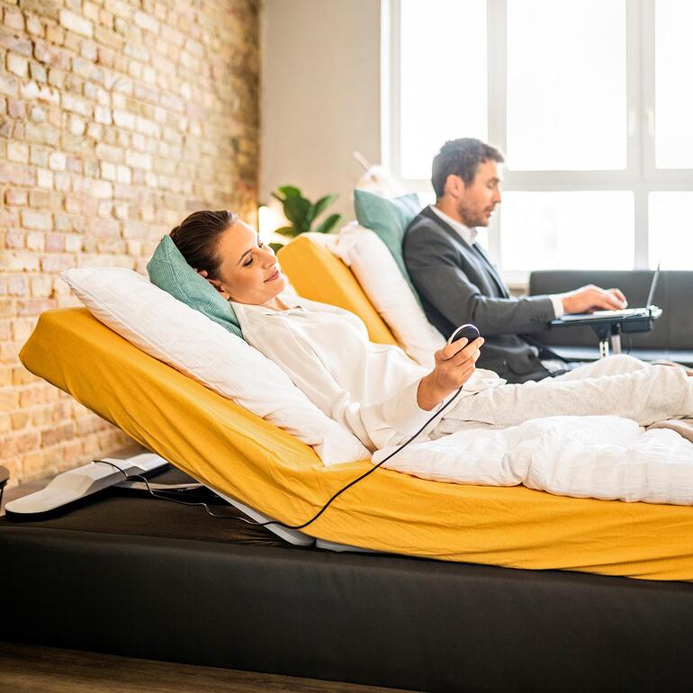 Vrouw en man zitten op een verstelbaar bed en praten met elkaar.
