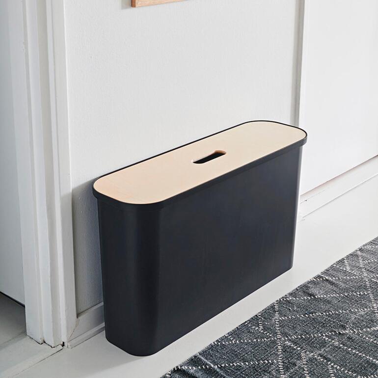 Zwarte opbergcontainer met een lichte deksel, tegen een muur geplaatst.