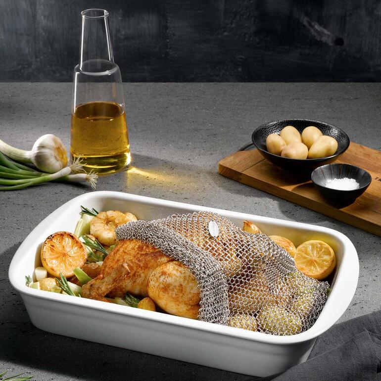 Kip in een braadnet op een bakplaat met groenten en olie.