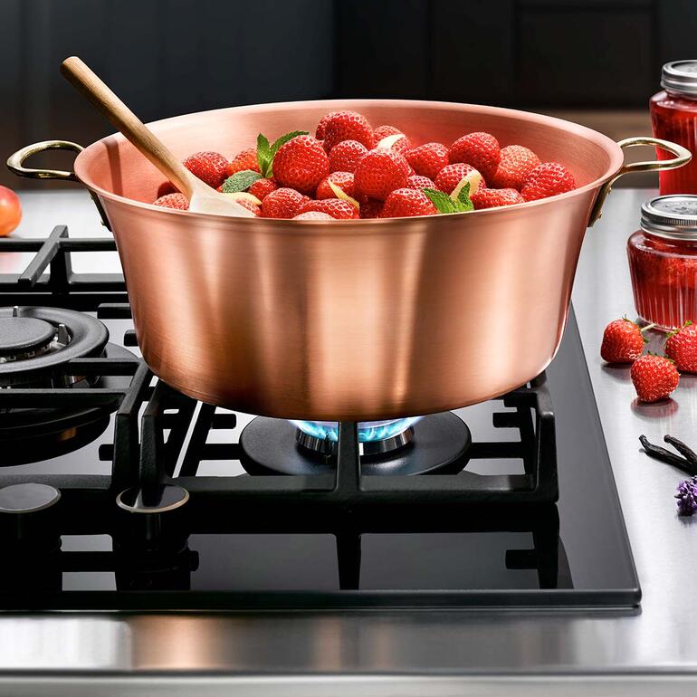 Koperen pot met verse aardbeien op het fornuis met een houten lepel.