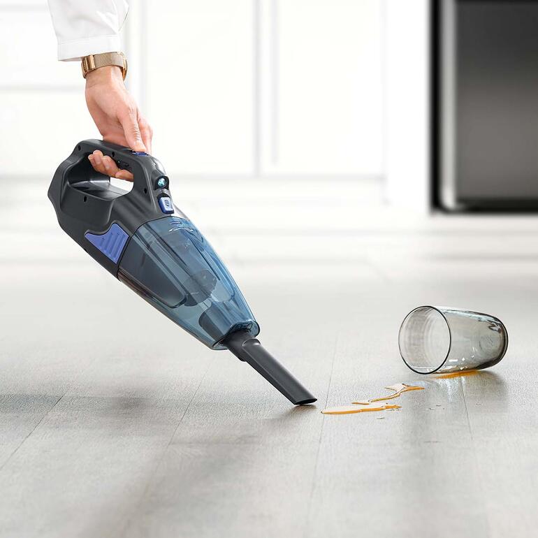 Moeiteloos en snel verwijdert de krachtpatser ook plassen gemorste vloeistoffen en vochtig vuil. Accu-handstofzuiger in de hand, zuigt gemorste sap op een houten vloer.