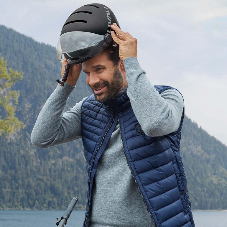 Het succesmodel met een cool, urban ontwerp is nu ook nog eens uitgerust met een vizier. Man zet een Livall L23 E-bike helm op zijn hoofd op de bergtop.