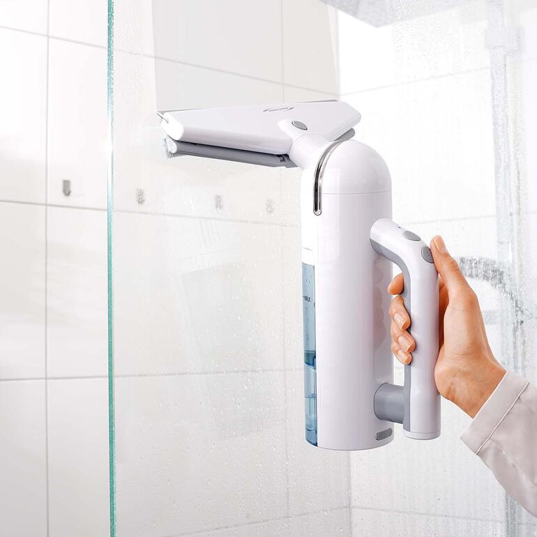 Hand houdt een witte accu-vensterreiniger vast in een badkamer.