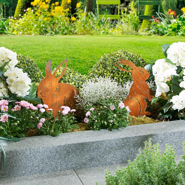 Twee metalen tuinprikkers in de vorm van konijnen geplaatst in een bloembed.