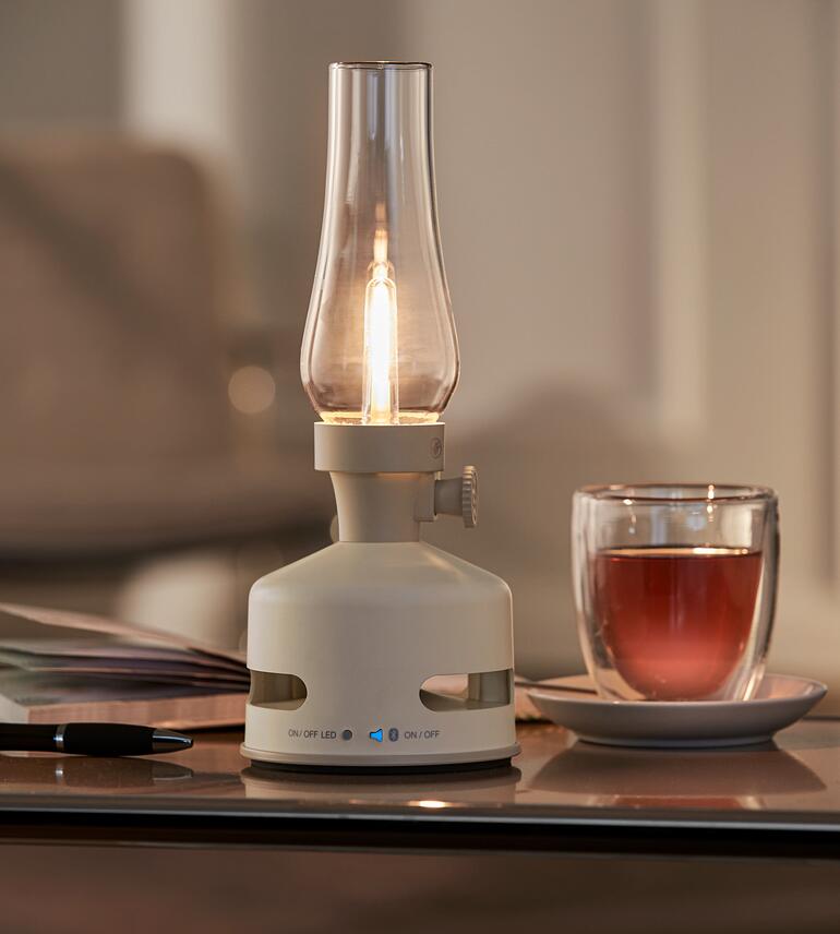 Met geïntegreerde Bluetooth-luidspreker voor een rustgevend en sfeervol geluid. LED olie lamp in crèmekleur op een tafel met een glas thee.