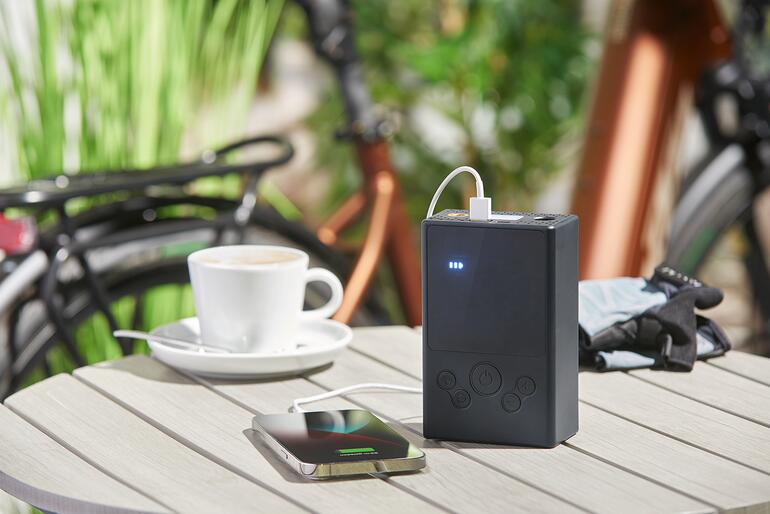 Ook een lithium-ion powerbank van 5.400 mAh voor mobiele telefoons, tablets en andere mobiele apparaten. Accu-compressor-luchtpomp laadt een smartphone op een tafel.