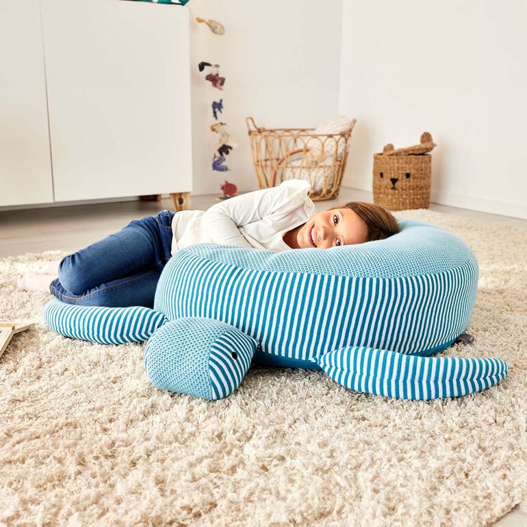 Op de 70 (!) cm hoge schildpadrug liggen kinderen heerlijk comfortabel. Meisje ligt op een knuffel-/zit schildpad en glimlacht naar de kamer.