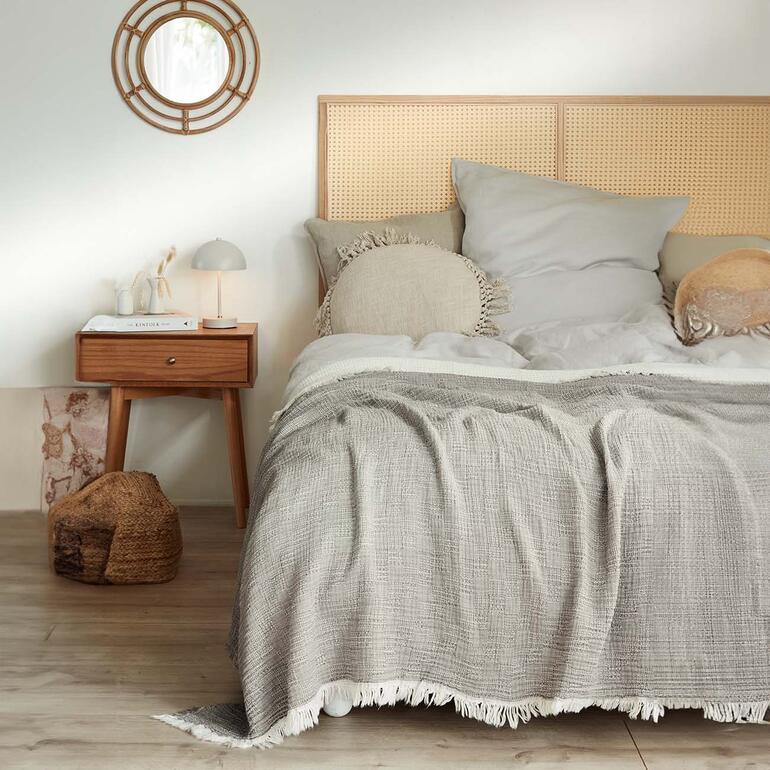 Ook ideaal als lichte sprei op bed. Musselindecke in grijs op een bed met hoofdbord en kussens.