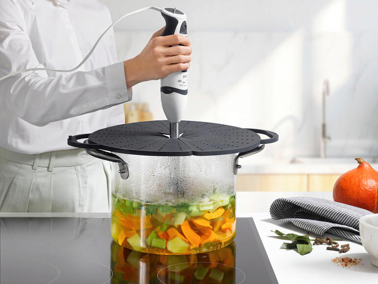 Vrouw pureert groenten in een pan met een siliconen spatscherm.