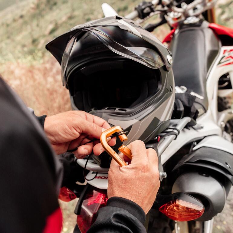 Persoon bevestigt een karabijnhaak met slot aan een motorhelm.