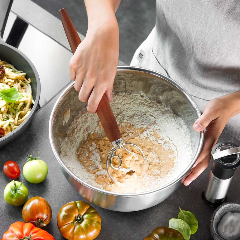 Handen gebruiken een Deens garde in een kom met deeg.