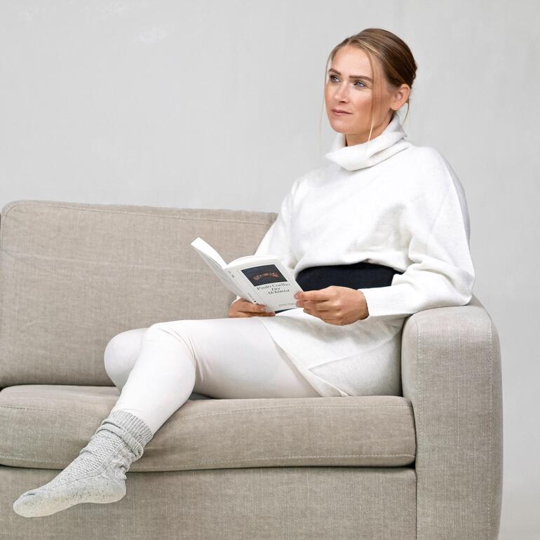Met comfortabele elastische band in 2 maten (veenkussen rug & buik). Vrouw met moorkussen om haar middel, leest een boek