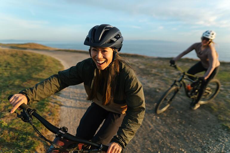 Groepen (fietsers) van elke grootte kunnen mondeling met elkaar communiceren – draadloos en met een glashelder geluid. Vrouw lacht op de fiets, draagt een helm met intercomsysteem.