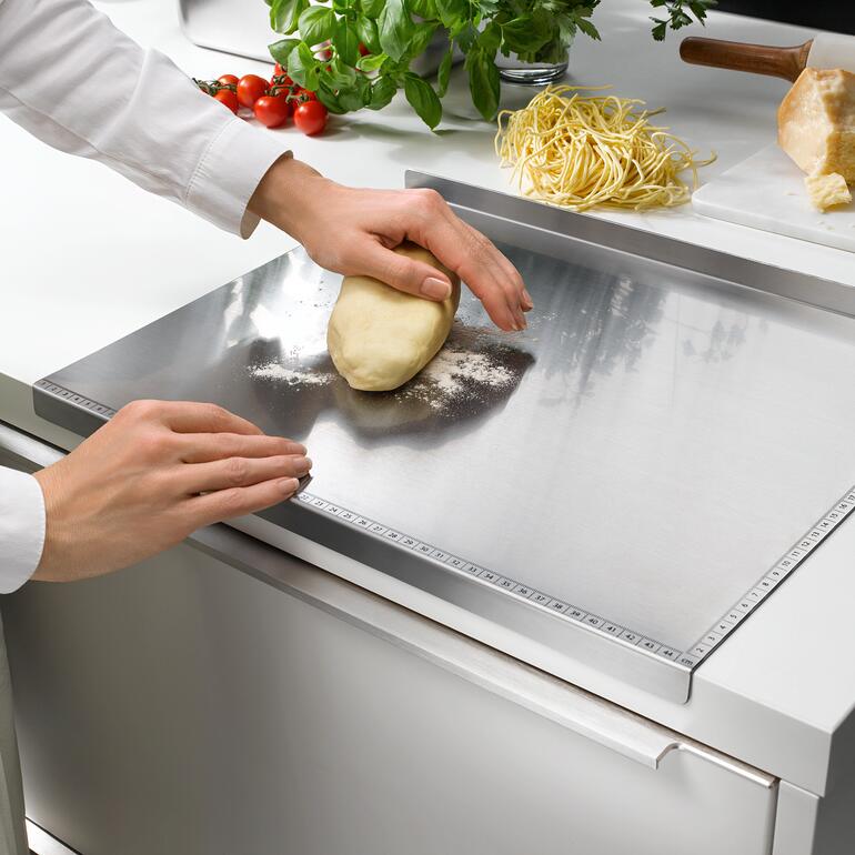 Persoon rolt deeg uit op een roestvrijstalen werkblad