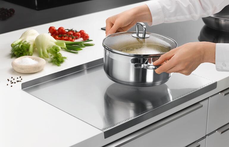Persoon tilt een pan met kokend water op een roestvrijstalen werkblad