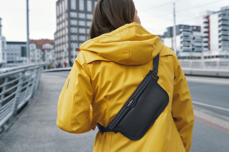 Vrouw in een gele jas draagt een zwarte crossbody tas over haar schouder.