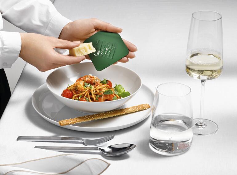 Persoon houdt Irogami designrasp boven een bord met pastasalade.