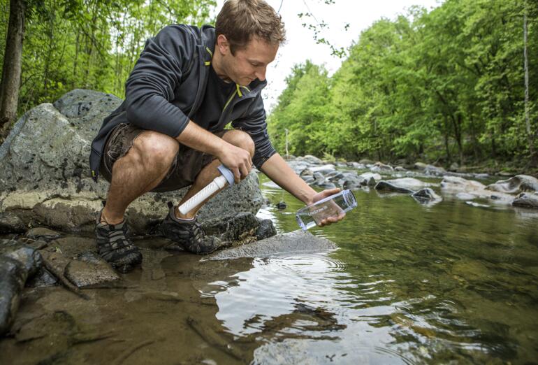 Man vult water uit een beek met een waterfilterfles