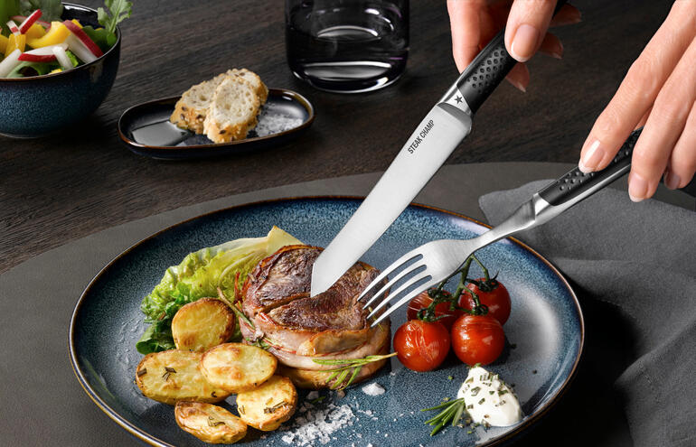 Hand die met steakbestek Prime Rib op een bord in een stuk steak snijdt.
