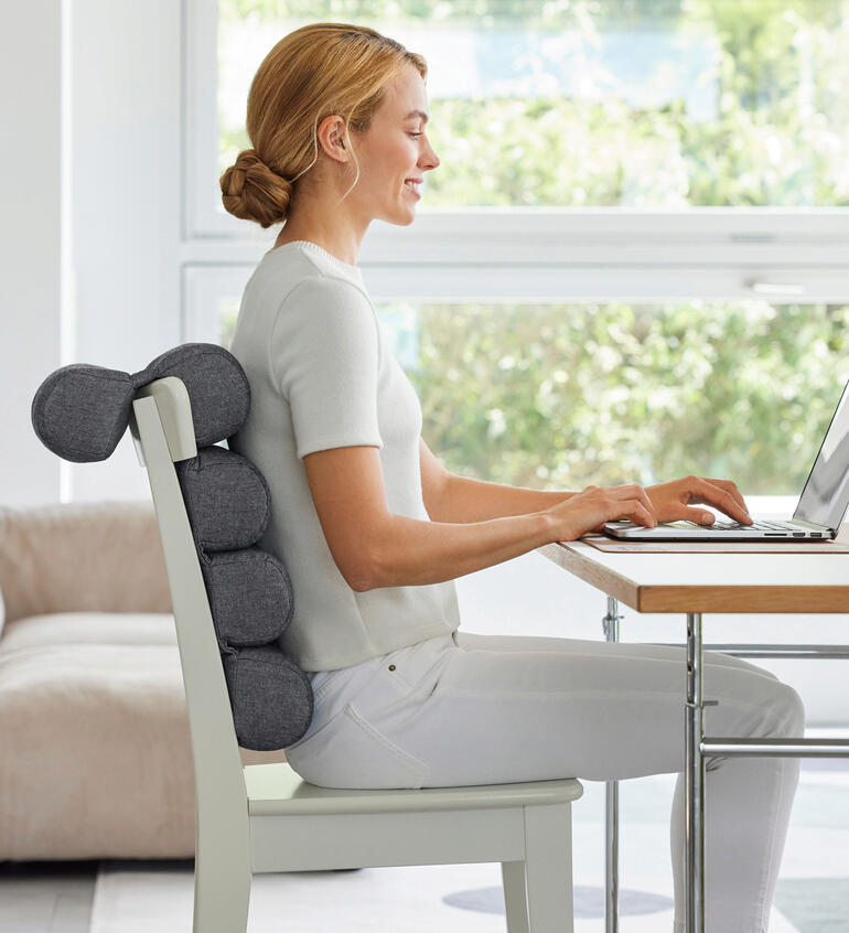Vrouw zit met flexi-rolkussen aan een bureau en werkt op de laptop.