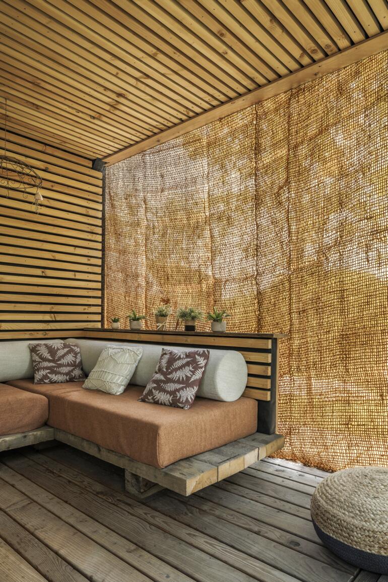 Kokosvezel is van nature weerbestendig en trek- en slijtvast. Vierkante zonnescherm van kokosvezels aan een houten muur in een gezellige zithoek.