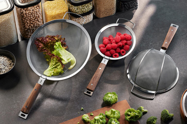 Drie zeefjes met houten handvatten op een keukentafel.