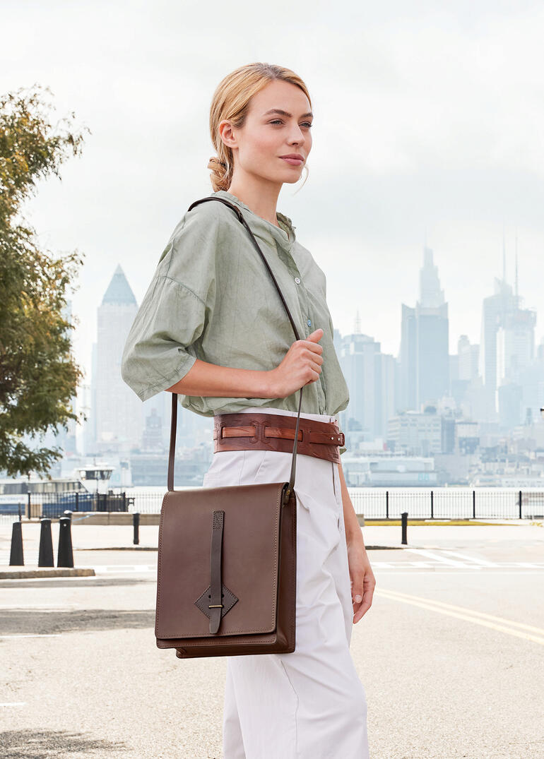 Vrouw draagt een bruine Chiarugi-kaartentas over haar schouder voor een stadszicht.
