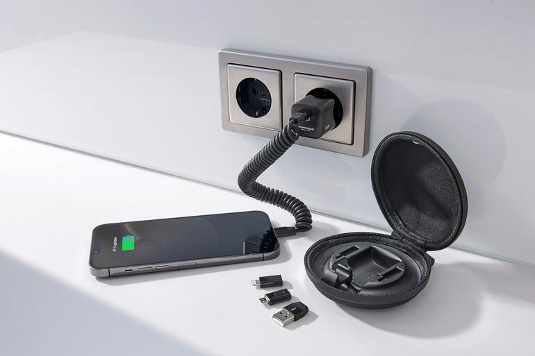 Smartphone, oplader en accessoires op een tafel, omgeven door een wandcontactdoos.
