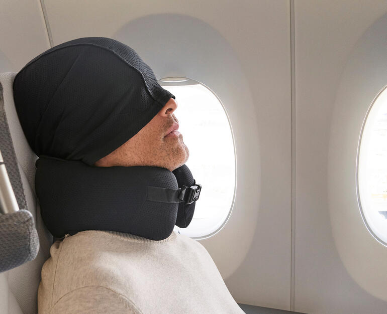 Comfortabel reiskussen met capuchon Man met een comfortabel reiskussen en kapuze in een vliegtuig
