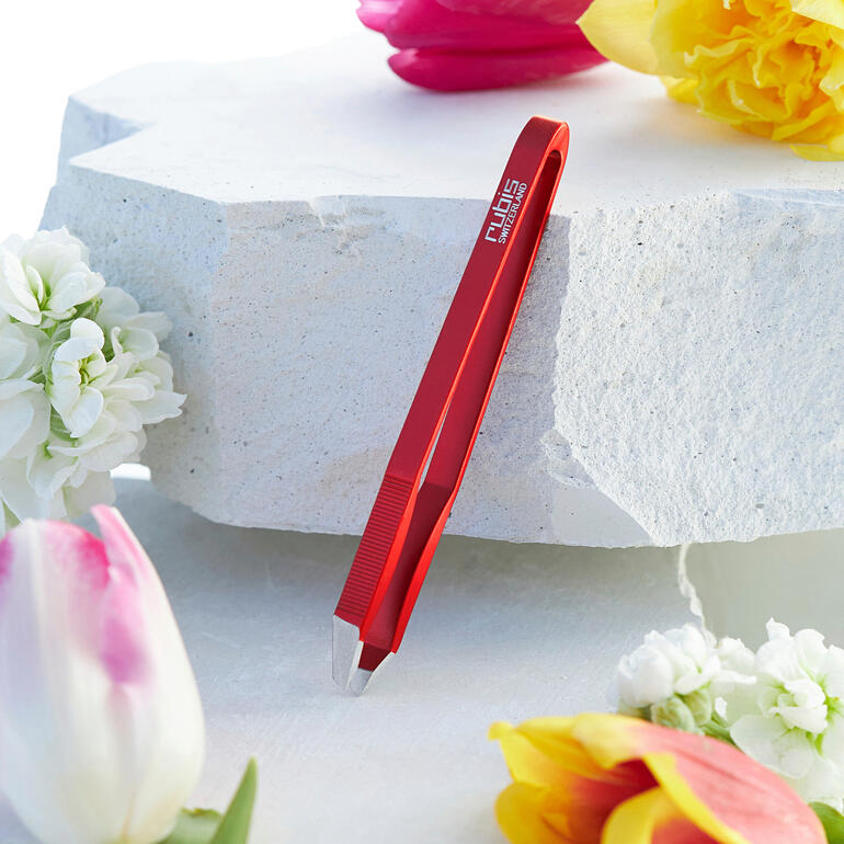 Ultraleichte pincet in rood, geplaatst op een witte stenen ondergrond, omringd door bloemen.