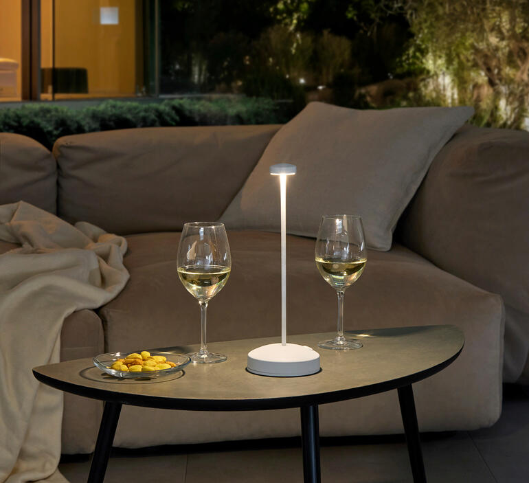 Design tafellamp met batterij op een tafel, omringd door wijnglazen en snacks.