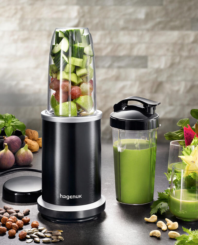 Smoothie-blender met fruit en groenten in de kom en een beker ernaast