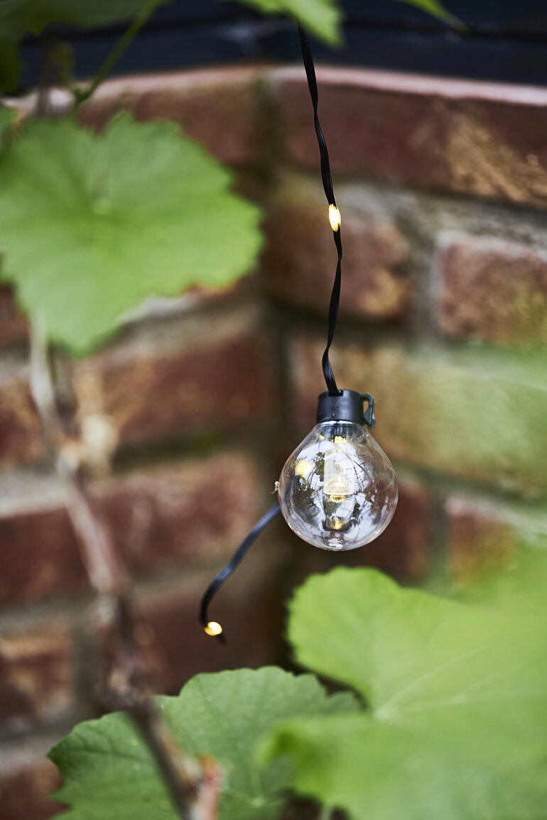 U kunt kiezen uit 8 verschillende functies – bijv. permanente verlichting, flashlight of subtiel knipperend. Close-up van een enkele gloeilamp van de lichtsnoer tussen planten.