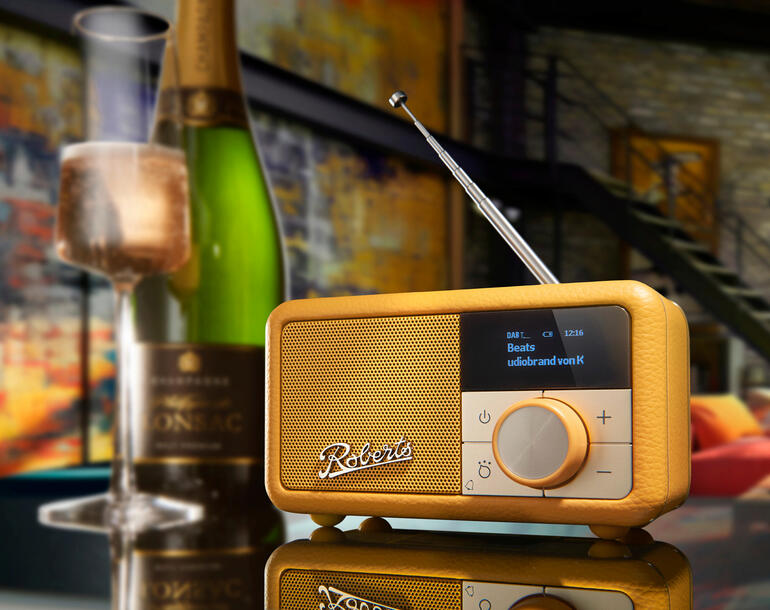 Roberts Revival Petite 2 radio op een tafel met champagne op de achtergrond
