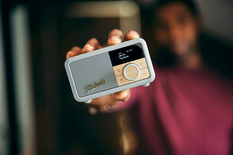 Man draagt mintgroene Roberts Revival Petite 2 tafelradio in zijn hand.
