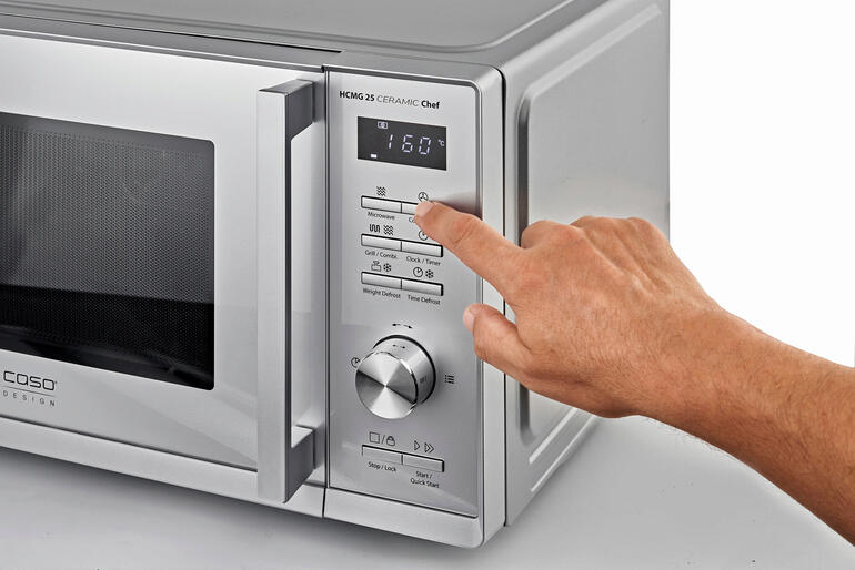 Selecteer eenvoudig met één druk op de knop het gewenste kookprogramma en het intelligente automatische systeem zorgt voor een perfect resultaat. Hand drukt op het bedieningspaneel van een 3-in-1 magnetron.