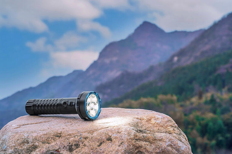 Bidirectionele 5000 lumen zaklamp op een steen met berglandschap op de achtergrond.