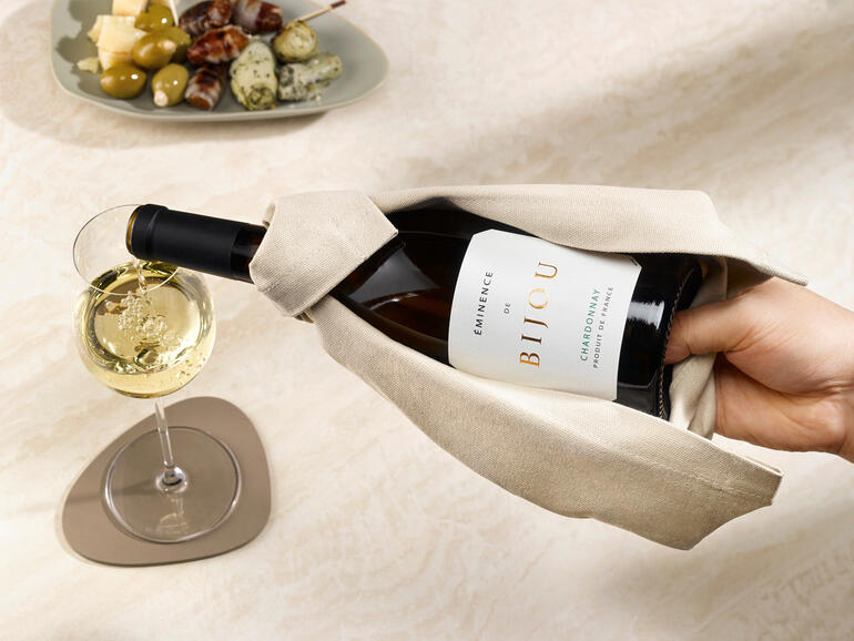 Tijdens het inschenken ligt de fles stevig in uw hand en druppelt er niks op tafel. Hand die een fles wijn uit de wijncape haalt.