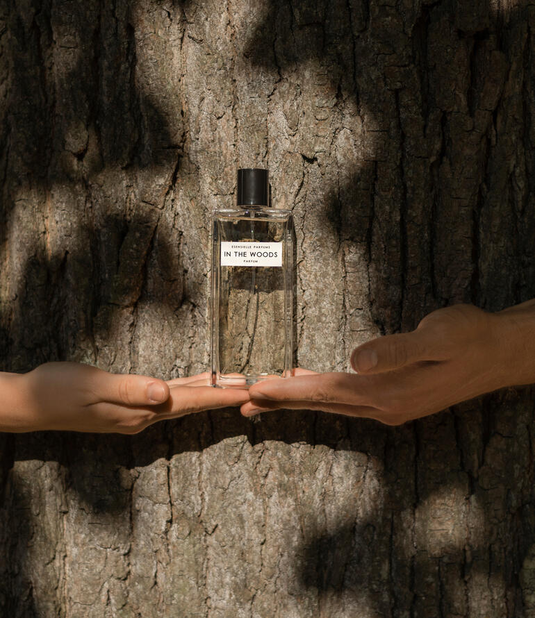 Fles In the Woods Eau de Parfum in handen, voor een boomschors.