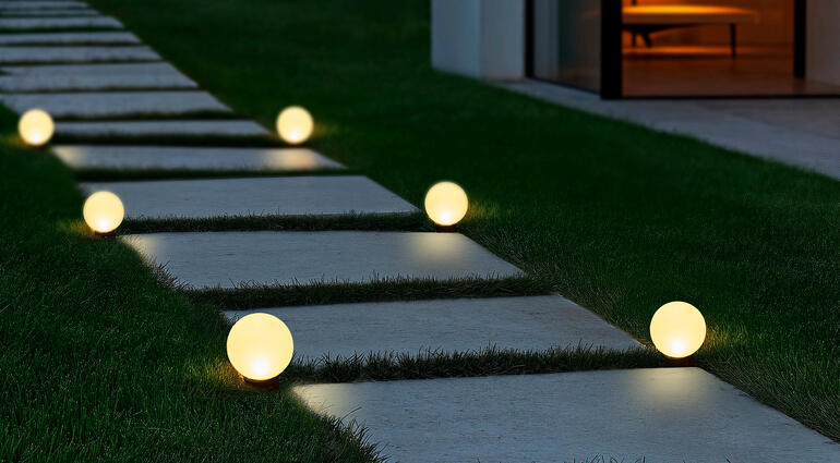 Per meegeleverde grondspies plaatst u de solarlampen langs een pad, in het bloemperk, in balkonbakken enz. Globe solar-lampen op een pad, verlicht en leidend naar een modern gebouw.