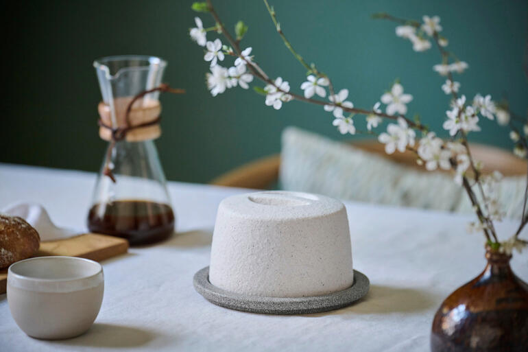 Keramische botervorm op een tafel met bloemen en koffiepot.