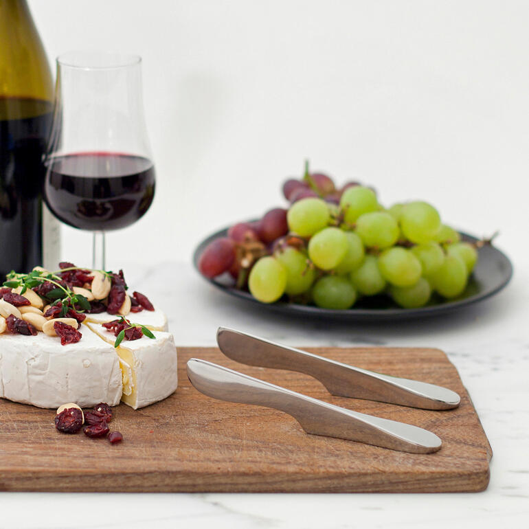 Set van twee zwevende smeermessen op een houten plank met kaas en druiven.