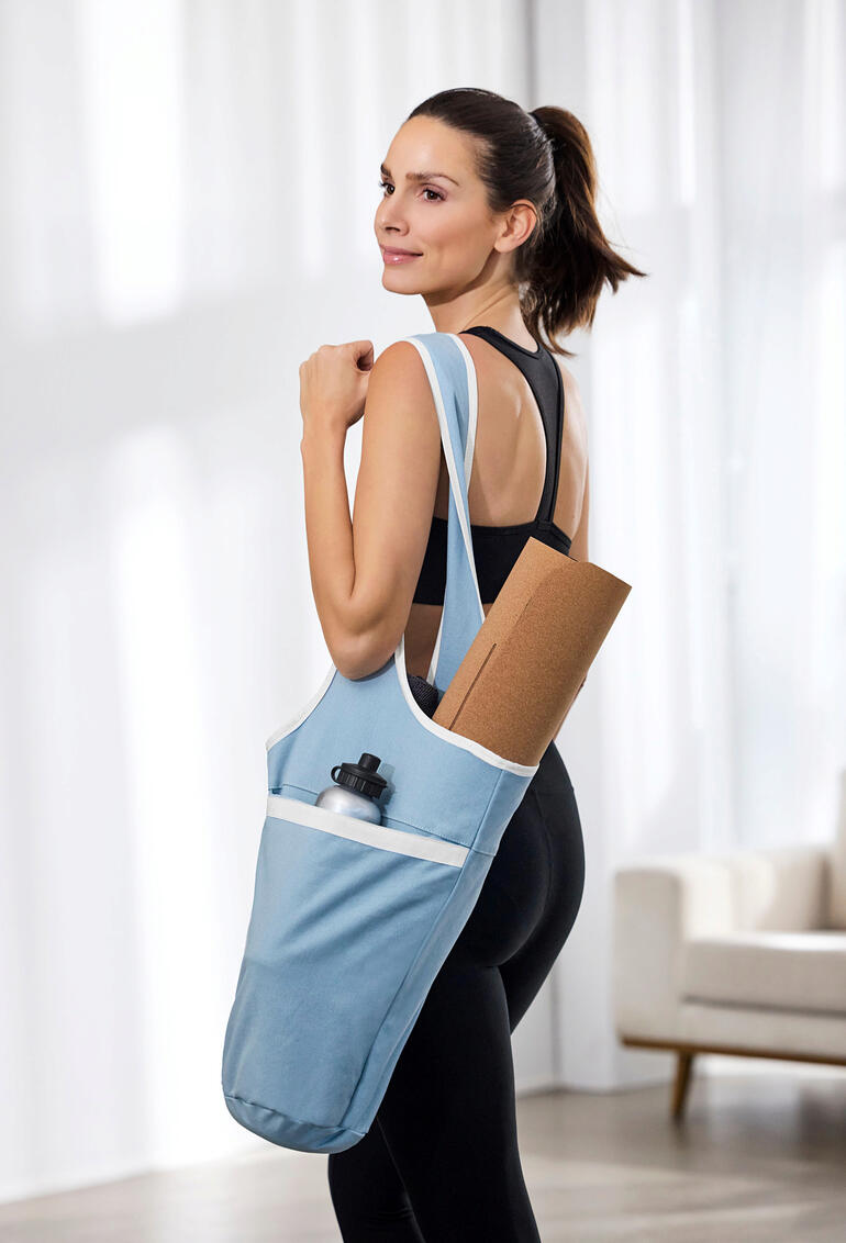 Vrouw draagt yogatas met yogamat en waterfles.