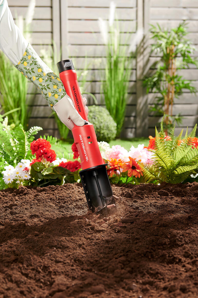 Accu-tuinboor Accu-tuinboor in de aarde met bloemen op de achtergrond
