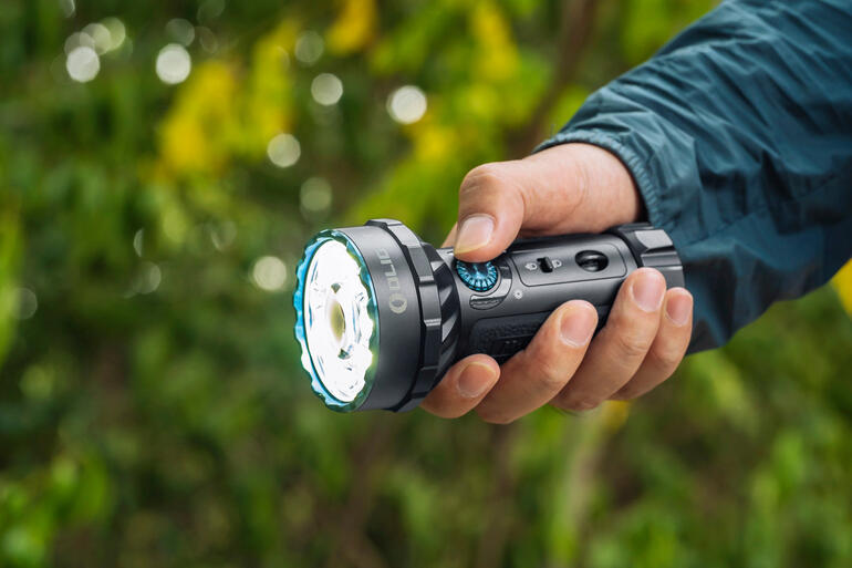 Intuïtief schakelbaar met de druk van uw duim. Man houdt een zaklamp vast in de buitenlucht met een groene achtergrond.