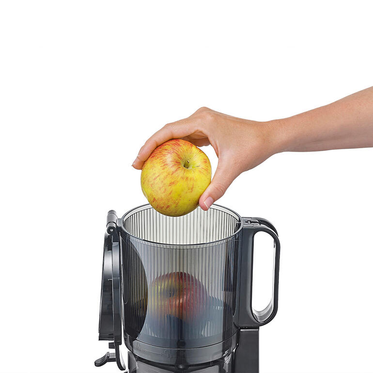 Hand die een appel in het bovenste vak van de CASO Slow-Juicer legt