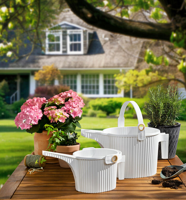 Twee gieters in wit en bloemen op een tafel in de tuin